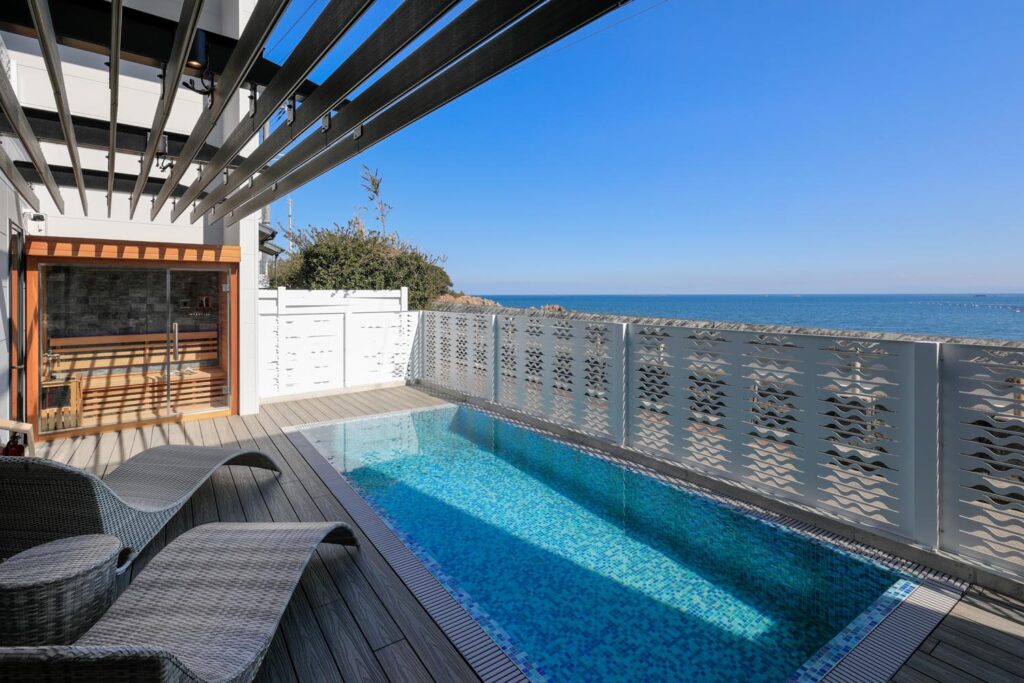 海が見える開放的なテラス。屋外用のテーブルと椅子、ラウンジチェアが配置されている