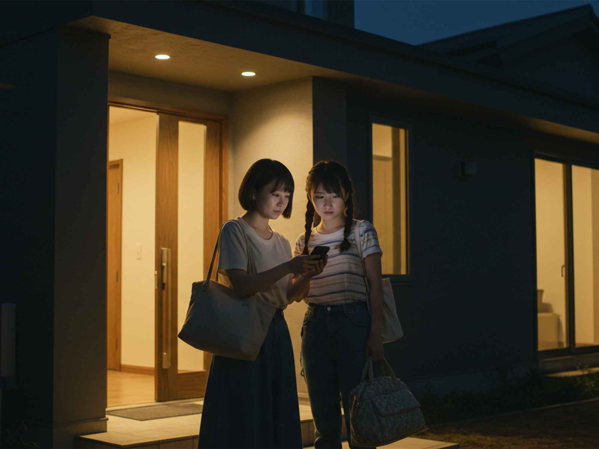 夜間のセルフチェックイン玄関先でコードを確認する女性