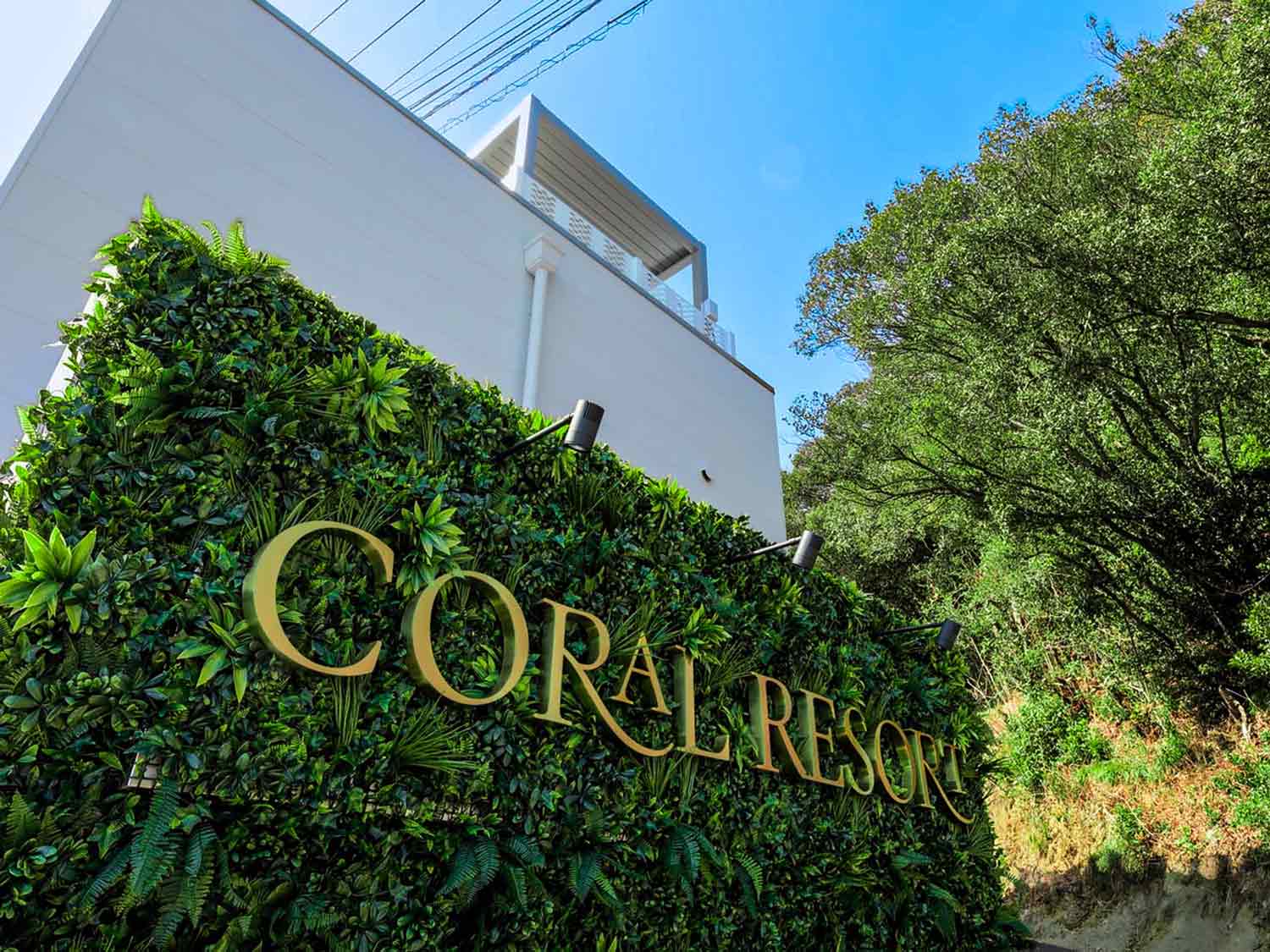 CORAL RESORT VILLA atsuhamaのグリーンウォール看板と青空のエントランス