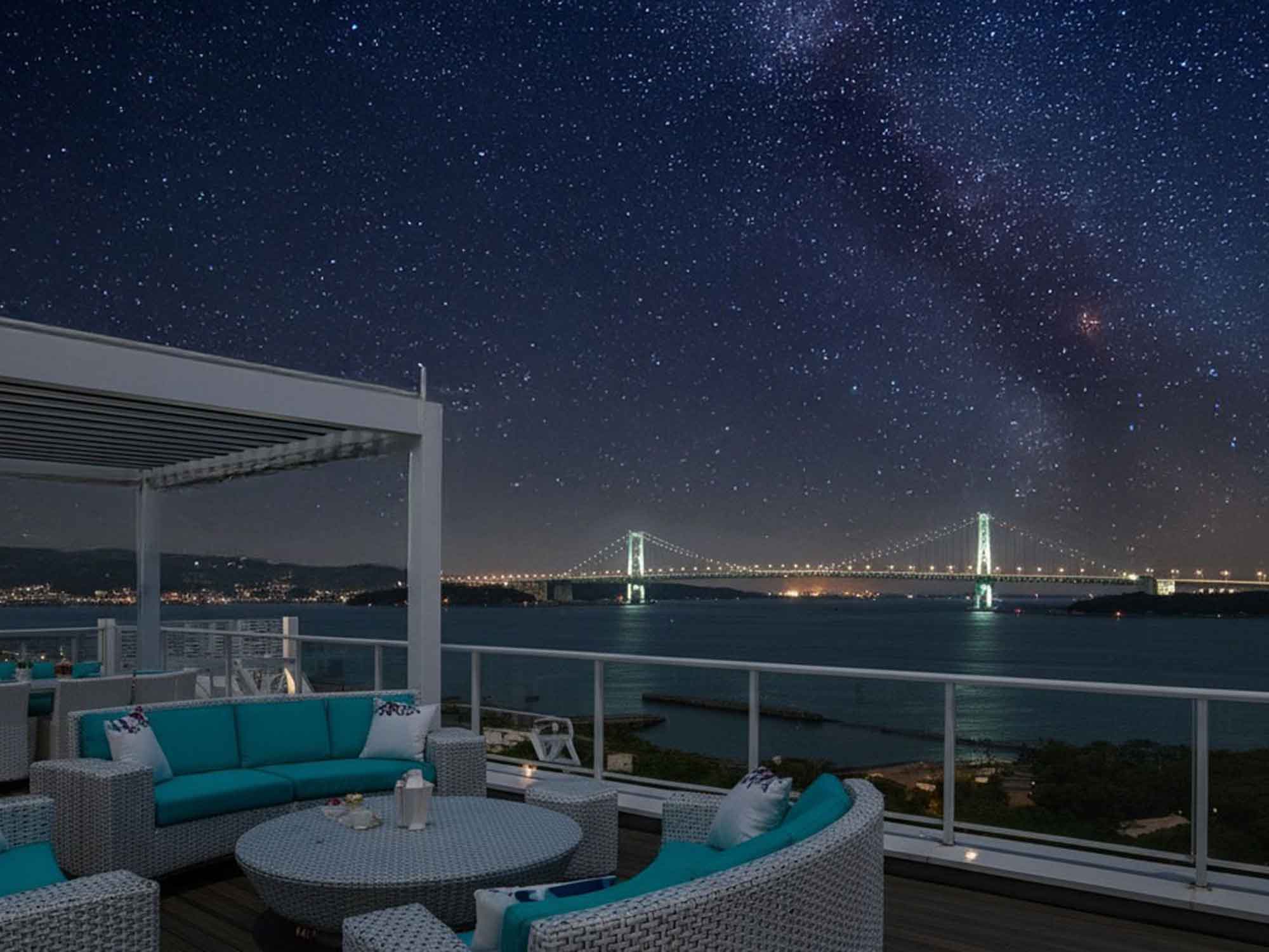 淡路島の屋上テラス付きヴィラから眺める明石海峡大橋と満天の星。ゆったりとしたソファで星空を楽しむロマンチックな夜の過ごし方。