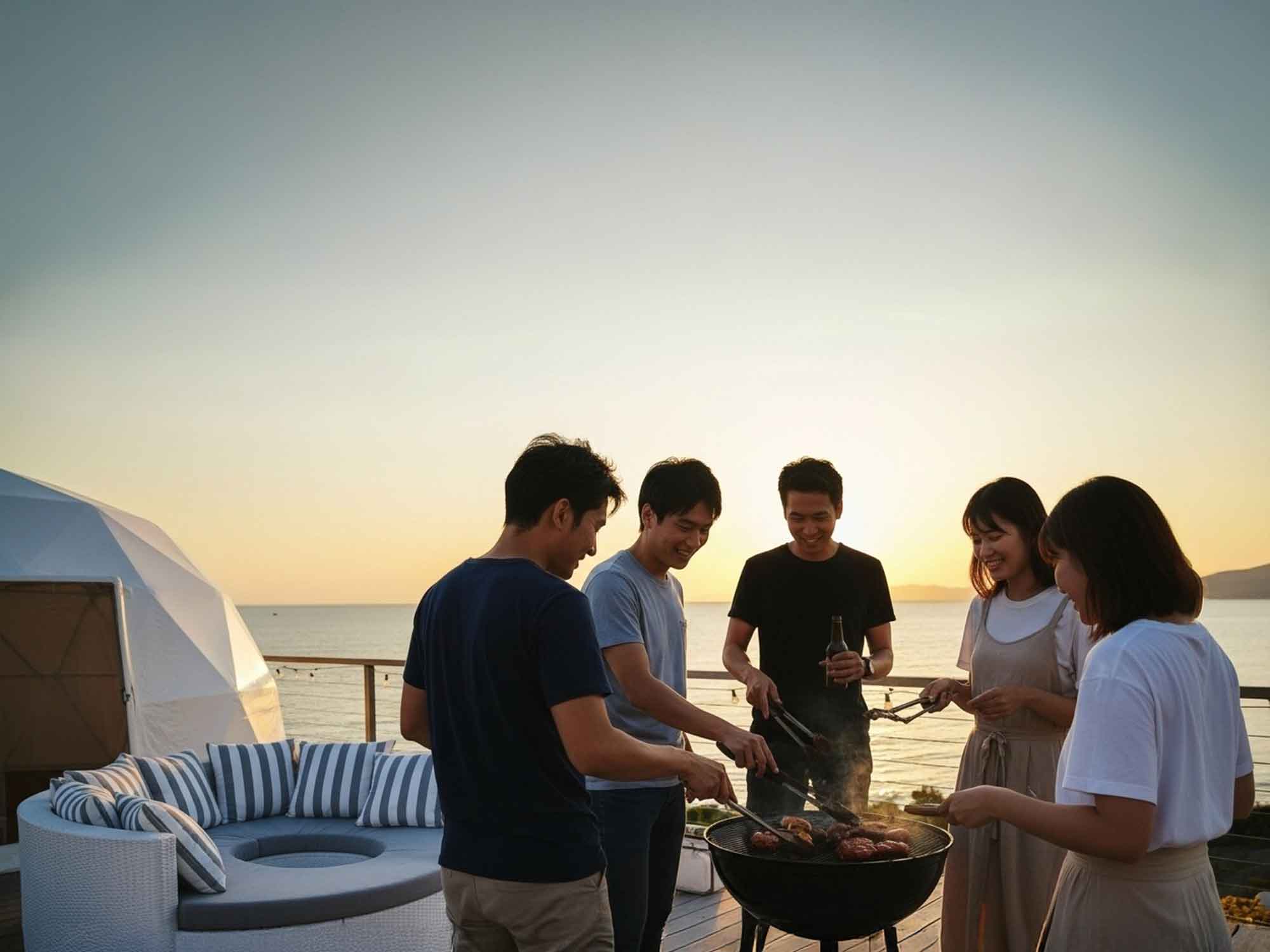 夕日を眺めながら友達と泊まるヴィラでBBQを楽しむ様子。海を背景にしたテラスで笑顔のグループ旅行。